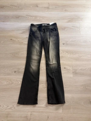 Svarta bootcut jeans med slitningar - Säljer ett par svarta bootcut jeans med snygga slitningar och ljusare partier framtill. Jeansen har klassisk femficksmodell och normal midja. Perfekta för dig som gillar en avslappnad men trendig look.