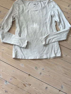 Vit långärmad topp från 157 - En enkel och stilren vit långärmad topp från 157. Tillverkad i mjuk bomull med rund halsringning och normal passform. Perfekt basplagg att matcha till olika outfits.