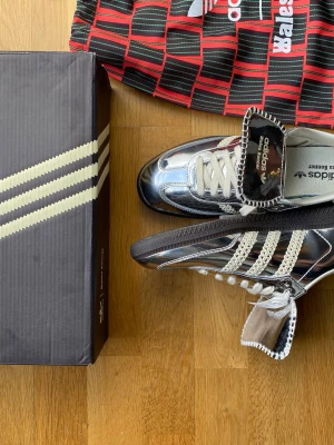 Adidas Wales Bonner silvriga sneakers - Snygga sneakers från Adidas x Wales Bonner i spegelblankt silver med vita detaljer och svarta sulor. Skorna har klassiska tre ränder i vitt, unika virkade detaljer och Wales Bonner-logga på sidan. Perfekta för dig som vill sticka ut med en futuristisk look.