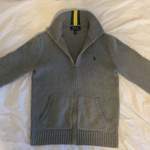 Ralph Lauren Stickad ”Brasilien” Cardigan - Säljer denna feta stickade Cardigan Från Ralph Lauren. Brasilien-inspirerade modell. Mycket gott skick utan defekter, knappt använd. Storlek L (14-16), men sitter ungefär som en XS i vuxenstorlek (kolla måtten innan du köper). Mått: Längd från Axel Och ner: 54 cm, Bredd under armhålorna: 46 cm