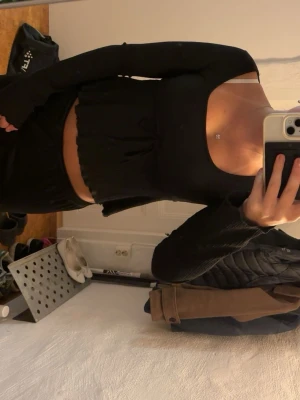Svart croppad topp från Nelly - Säljer en svart croppad topp från Nelly med lång ärm och fyrkantig ringning. Toppen är ribbad och har en tight passform som framhäver midjan. Perfekt att styla med höga jeans eller kjol.