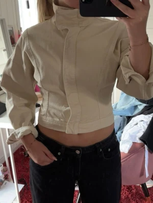 Beige croppad jacka med hög krage - Säljer en beige croppad jacka med hög krage och långa ärmar. Använd ett fåtal gånger. 