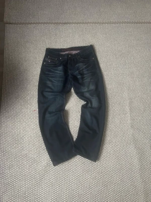 Tommy hilfiger  - Säljer ett par Tommy hlifiger jeans med raka ben och snygga slitningar framtill. Jeansen har klassisk femficksmodell och kontrastsömmar. Perfekta för en avslappnad och trendig look.