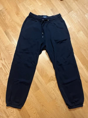 Svarta mjukisbyxor H&M - Säljer ett par bekväma svarta mjukisbyxor från H&M med dragsko i midjan och resår vid bensluten. Byxorna har två sidofickor och är gjorda i mjukt bomullsmaterial. Perfekta för chill dagar eller när du vill vara extra bekväm. Vid frågor, extra bilder eller liknande är det bara att kontakta mig!