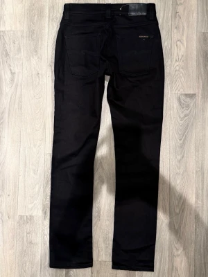 Nudie Jeans Grim Tim Svarta W29/L32 - Slim Straight Fit - Nudie Jeans Grim Tim ”Black Ring” svarta jeans med slim straight fit-passform, normal midja och raka ben, storlek W29/L32, midja 37 cm, ytterbenslängd 106 cm, benöppning 17 cm, modellen är 185cm & väger 65kg, i fint skick.