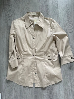 Beige skjorta  - Ny med lapp. Skick enligt bilder. Hjälper min mormor att sälja . De är av äldre modeller och märken.