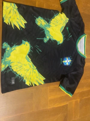 Svart Brasilien fotbollströja Nike - Säljer en svart Brasilien fotbollströja från Nike med stora gula fåglar och gröna detaljer. Tröjan har grönt och gult ribbstickat avslut vid hals och ärmar samt Brasilien-emblem på bröstet. Tillverkad i Dri-Fit material som andas.