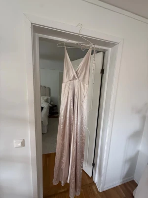 Champagnefärgad långklänning Bubbleroom - Säljer en elegant champagnefärgad långklänning från Bubbleroom i glansigt material. Klänningen har v-ringning, smala axelband och omlott upptill. Perfekt för speciella tillfällen och ger en lyxig känsla.🤍