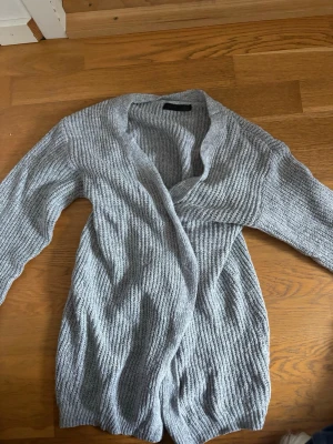 Ljusgrå stickad kofta - Mysig ljusgrå stickad kofta med ribbad struktur och lång ärm. Koftan har en avslappnad passform och öppen front, perfekt att slänga över en t-shirt eller topp. Tillverkad i mjukt material som känns skönt mot huden.