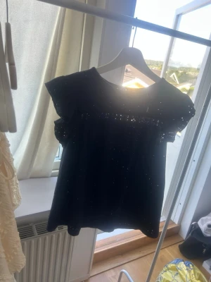 Mörkblå topp med volangärm - Söt mörkblå topp med broderade hål och volangärmar. Toppen har rund halsringning och ett luftigt, lätt material som ger en romantisk känsla. Perfekt för dig som gillar detaljer och en feminin stil.