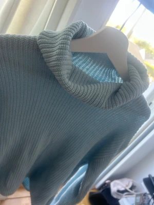Ljusblå stickad polotröja - Mysig ljusblå stickad polotröja med bred ribbstickning och lång ärm. Tröjan har en hög, vikt krage och är perfekt för kyliga dagar. Materialet känns mjukt och stretchigt, vilket gör den skön att bära.