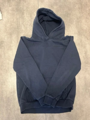 Mörkblå hoodie från Peak Performance - Snygg mörkblå hoodie från Peak Performance med klassisk huva och magficka. Tillverkad i mjukt material som känns skönt mot huden. Diskret logga på bröstet och ribbade muddar vid ärmar och nederkant. Perfekt för en chill och avslappnad stil.