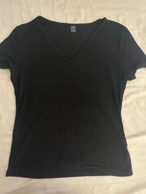 Svart v-ringad t-shirt - En enkel svart t-shirt med v-ringning och korta ärmar. Perfekt basplagg som passar till det mesta. Tillverkad i mjukt material för skön känsla hela dagen.