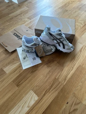 Asics gel kayano 14 - Snygga sneakers från Asics i vitt och silver med svarta detaljer. Skorna har en sportig design med meshpaneler för bra ventilation och robust sula för extra komfort. Perfekta för dig som gillar en clean och modern look.