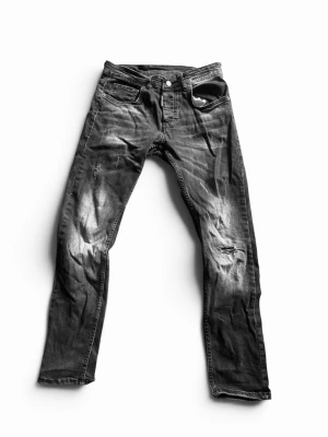 Svarta DSquared jeans med slitningar - Säljer ett par svarta skinny jeans från Dr. Denim med slitningar på benen och klassisk femficksmodell. Jeansen har en tvättad look och smal passform som sitter tight hela vägen ner. Perfekta för dig som gillar en edgy stil.