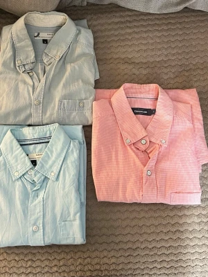 Två ljusblå och en rosa skjorta - Tre kortärmade skjortor i klassisk modell, två i ljusblått och en i ljusrosa med diskret rutmönster. Alla har knappar framtill och krage. Perfekta för en clean och stilren look.