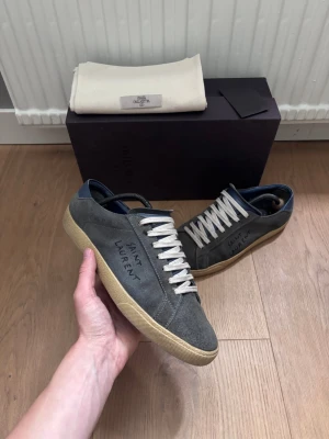 Saint Laurent mocka sneakers - Tja, säljer nu ett par Saint Laurent 06 Classic Court i färgen navy. Väldigt ovanliga, köpta utomlands. Skorna är i storlek 43 och de är i hyfsat skick. Skorna ingår samt en Saint Laurent dust bag för snörena. Vid frågor eller fler bilder är det bara att höra av sig.
