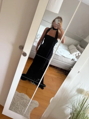 Svart långklänning med halterneck - Säljer en elegant svart långklänning med halterneck och öppen rygg. Klänningen har en figurnära passform och faller snyggt längs kroppen. Perfekt för dig som vill ha en stilren och klassisk look.