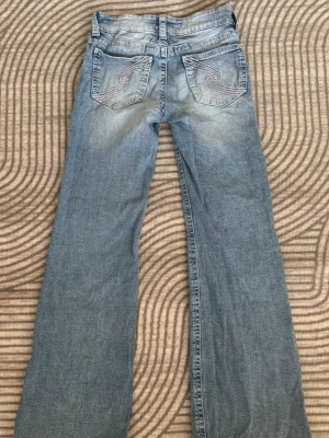 Ljusblå Gina tricot bootcut jeans  - Säljer ett par ljusblå bootcut jeans med snygga detaljer på bakfickorna. Jeansen har en klassisk femficksmodell och är tillverkade i denim med lätt slitna partier framtill och baktill för en cool vintagekänsla.