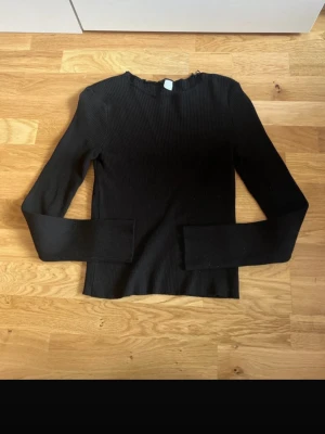 Svart ribbad långärmad topp - Säljer en svart långärmad topp med ribbad struktur och rund hals. Toppen har en enkel och stilren design som passar till det mesta. Perfekt att matcha med jeans eller kjol för en clean look.