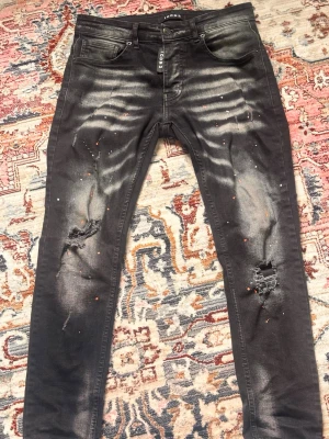 Svarta skinny jeans med slitningar - Snygga svarta skinny jeans med slitningar på knäna och blekta detaljer framtill. Jeansen har även små färgstänk och klassisk femficksdesign. Perfekta för en edgy streetstil och tillverkade i stretchigt denimtyg.