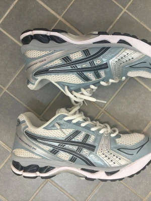 Ljusblå och vita Asics sneakers - Säljer ett par fräscha Asics sneakers i ljusblått och vitt med svarta detaljer. Skorna har meshpaneler för bra ventilation och klassisk snörning. Snygg retrostil med bekväm sula, perfekta för dig som gillar sportig look.
