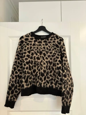 Leopardmönstrad stickad tröja NA-KD - Säljer en stickad tröja från NA-KD med leopardmönster i beige och svart. Tröjan har rund halsringning, långa ärmar och svarta ribbade muddar vid ärmslut och nederkant.