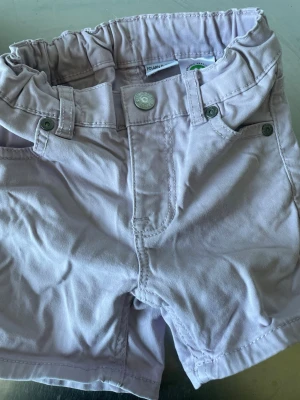 Ljuslila shorts från Polarn O. Pyret - Säljer ett par ljuslila shorts från Polarn O. Pyret i mjuk ekologisk bomull. Shortsen har resår i midjan, knapp och bälteshällor samt två fickor fram. Perfekta för varma dagar och riktigt sköna att bära.