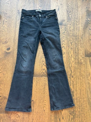 Svarta bootcut jeans från Kappahl - Snygga svarta bootcut jeans från Kappahl och normal midja. Jeansen har utsvängda ben och är tillverkade i ett mjukt denimtyg med lite stretch för extra komfort. Perfekta för en trendig och avslappnad look.
