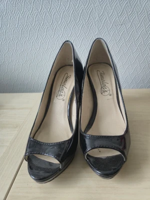 Svarta peep toe pumps från Timeless - Snygga svarta pumps med peep toe och hög klack från Timeless. Skorna har en glansig finish i lackmaterial och klassisk siluett som ger en elegant look. Perfekta för att lyfta vilken outfit som helst.