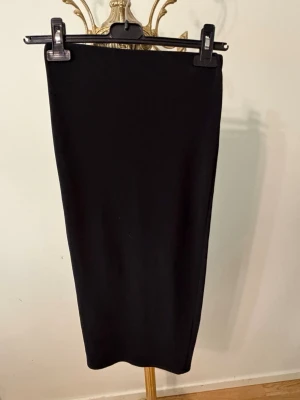 Svart långkjol med slits, Zara 38. - En stilren svart långkjol med rak passform och diskret slits bak. Kjolen är enkel och tidlös, perfekt att matcha med olika toppar. Materialet ser ut att vara mjukt och stretchigt, vilket ger en bekväm känsla.