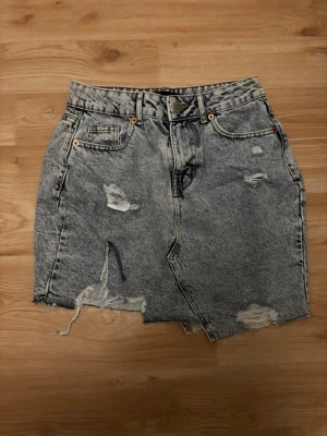 Grå jeanskjol med slitningar - Snygg grå jeanskjol med slitna detaljer och rå kant nertill. Kjolen har klassisk femficksdesign och hög midja. Perfekt för en avslappnad och trendig look.