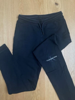 Svarta mjukisbyxor Calvin Klein  - Snygga svarta mjukisbyxor från Calvin Klein Jeans med broderad logga på knäet. Byxorna har dragsko i midjan och smal passform. Perfekta för chill dagar eller när du vill ha en clean och enkel look. Den är lite blekt vid midjan men inget som syns 🫶🏻