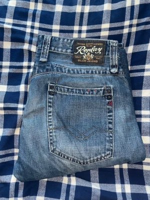 Replay jeans  - Säljer ett par klassiska blå jeans från Replay med raka ben och snygga slitningar. Jeansen har fem fickor, detaljerade sömmar och en patch med Replay-loggan bak i midjan. Tillverkade i slitstark denim som ger en cool och avslappnad look.. JAG SKICKAR EJ FLER BILDER NÄR JAG BÄR JEANSEN! för bättre inblick i passformen rekommenderar jag att googla på modellnamnet. För storleksguide kolla måtten noggrant då jeansen alltid kan vara uppsydda heller krympta och jag ej tar emot returer :) s6,2