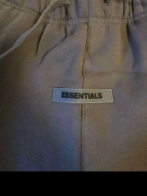 Gråa Essentials shorts med snörning - Snygga Gråa shorts från Essentials med elastisk midja och snörning. De har en enkel design med en bakficka och Essentials-logga framtill. Perfekta för chill dagar och sommarhäng.