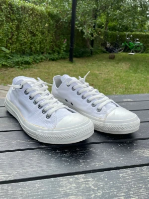 Vita Converse All Star låga sneakers - Klassiska vita Converse All Star sneakers i canvas med vita snören och gummisula. Skorna har metallfärgade öljetter och låg profil som ger en clean och tidlös look. Perfekta för dig som gillar streetstyle och vill ha ett par ikoniska sneakers i garderoben.