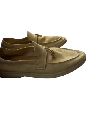 Loro piana ÄKTA loafers - Äkta,  Storlek 39,5 Köpta via Vestiaire Collective Mockan har behållit sin mjuka textur och nyansen varierar naturligt. Lätta tecken på användning syns, särskilt vid tårna och på sidorna. Det finns visst slitage på in- och yttersulor, samt normalt användningsslitage på klackarna och sulkanterna. Jag säljer dem eftersom de var för stora för mig i hälen. Vänligen kontrollera tillgängligheten innan köp, då skorna även ligger ute till försäljning på andra plattformar.
