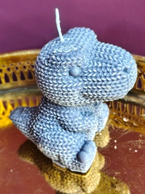 Blå dinosaurieformad ljus - Unik dekoration i form av ett blått dinosaurieljus med stickad look. Ljuset är detaljerat med struktur som liknar virkat garn och har en söt, rundad form. Perfekt som rolig inredningsdetalj eller present till någon som gillar dinosaurier.