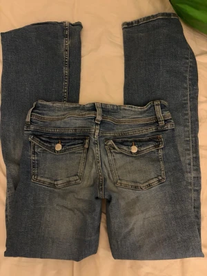 Low waist bootcut jeans - Snygga blå jeans från Gina Tricot i klassisk modell med raka ben och två bakfickor med lock och knappdetaljer. Jeansen har en tvättad look och är tillverkade i mjukt denimtyg som passar perfekt till en avslappnad stil.