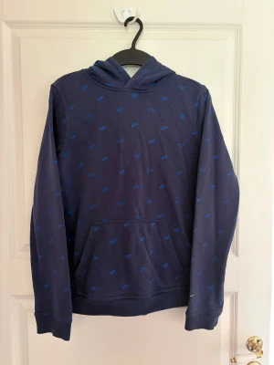 Mörkblå hoodie med Nike-loggor - Snygg mörkblå hoodie från Nike med all-over print av små blå Nike-loggor. Hoodien har en klassisk känguruficka framtill och huva. Perfekt för en avslappnad och sportig stil. Storlek: 158/170. Kolla gärna mina andra annonser❗️