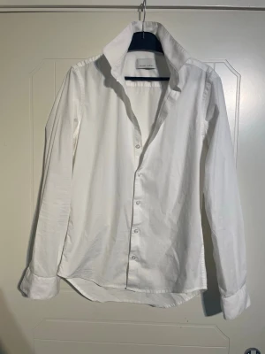 Vit skjorta från Casual Friday - Klassisk vit skjorta från Casual Friday med lång ärm och knappar framtill. Skjortan har en snygg krage och är tillverkad i mjuk bomull som känns skön mot huden. Perfekt att styla till olika outfits för en clean och fräsch look.