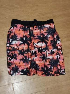 Färgglada badbyxor med palmtryck - INSTABOX!!! Säljer ett par riktigt snygga badbyxor med tropiskt palmtryck i svart mot en färgstark bakgrund i orange, rosa och vitt. De har svart midjeresår med snörning för bästa passform. Perfekta för stranden eller poolen!