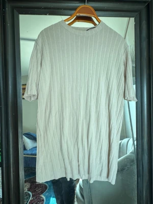 Beige ribbad topp med kort ärm - Säljer en beige ribbad topp med korta ärmar och rund hals. Toppen har en enkel och stilren design med vertikala ribbade ränder som ger en snygg struktur. Perfekt att matcha med jeans eller kjol för en clean look.