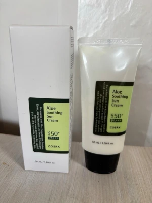 Set - COSRX Aloe Soothing Sun Cream SPF50+ - Aloe Soothing Sun Cream från COSRX med SPF50+ PA+++ skyddar huden mot solen och återfuktar med aloe vera. Kommer i en vit tub med svart lock och grön etikett. Innehåller 50 ml och passar perfekt för daglig användning. OBS! Antal  2 st
