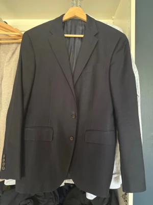 Ralph Lauren kavaj - Stilren mörkblå kavaj med två knappar framtill och klassisk krage. Kavajen har två fickor med lock och en bröstficka. Insidan är fodrad och har en innerficka med etiketten 'Custom Fit'. Perfekt för en dressad look. Kavajen ser bra skick ut, några defekter som e väldigt små på utsidan och lite på insidan av ena armen. Nypris runt 5000kr. Sitter bra på 175-183cm 