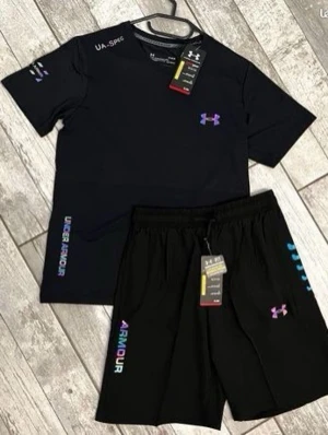 Svart träningsset från Under Armour - Snyggt svart träningsset från Under Armour med t-shirt och shorts. Setet har färgglada loggor och textdetaljer i lila, blått och rosa. Tillverkat i ett lätt och snabbtorkande material som passar perfekt till gymmet eller löpning.