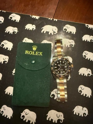Rolx GMT-Master II Root Beer - Snygg GMT-Master II med länk i roseguld och  svart urtavla, även den modell kallad för Root Beer. Klockan har tydliga index, datumfönster och vridbar bezel. Finns även extra länkar. Kommer med grön Rolx-fodral i mocka och även NFC-kort till specifika modellen.