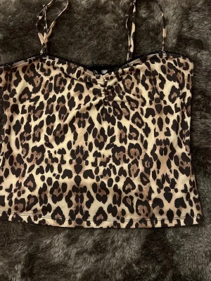 Leopardmönstrat topp med smala band och lång kjol  - Säljer ett leopardmönstrat topp med smala axelband och liten rosett framtill. Toppen har en beige och brun färgskala och är tillverkad i ett mjukt, glansigt material som känns lyxigt, kjolen är storlek xs och toppen är M men passar som S 