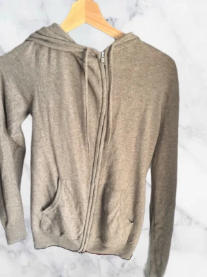 John Henric Zip up - Mysig beige hoodie med dragkedja framtill och två fickor. Modellen har huva med dragsko och långa ärmar. Tillverkad i mjukt, tunt material som passar perfekt för en avslappnad stil. Tyvärr en del hål så därav de låga priset ifrån va ny pris är. Lätt att sy hålen då synns det sedan knappt!