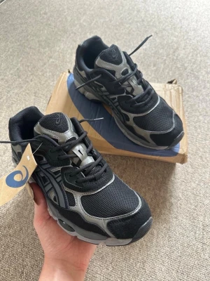  Asics gel nyc black - Snygga sneakers från Asics i svart och grått med meshpaneler och detaljer i mockaimitation. Skorna har en chunky sula och klassisk snörning. Perfekta för dig som gillar sportig och trendig stil.